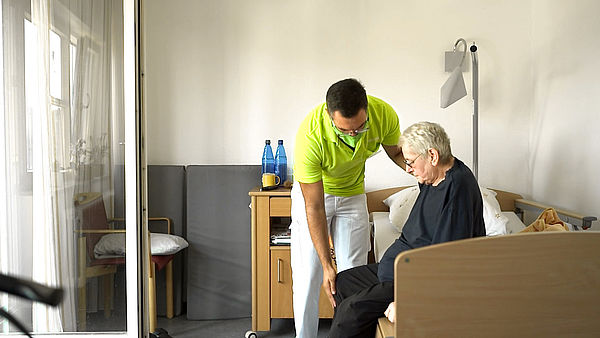 Pfleger assistiert älterem Menschen beim Aufstehen