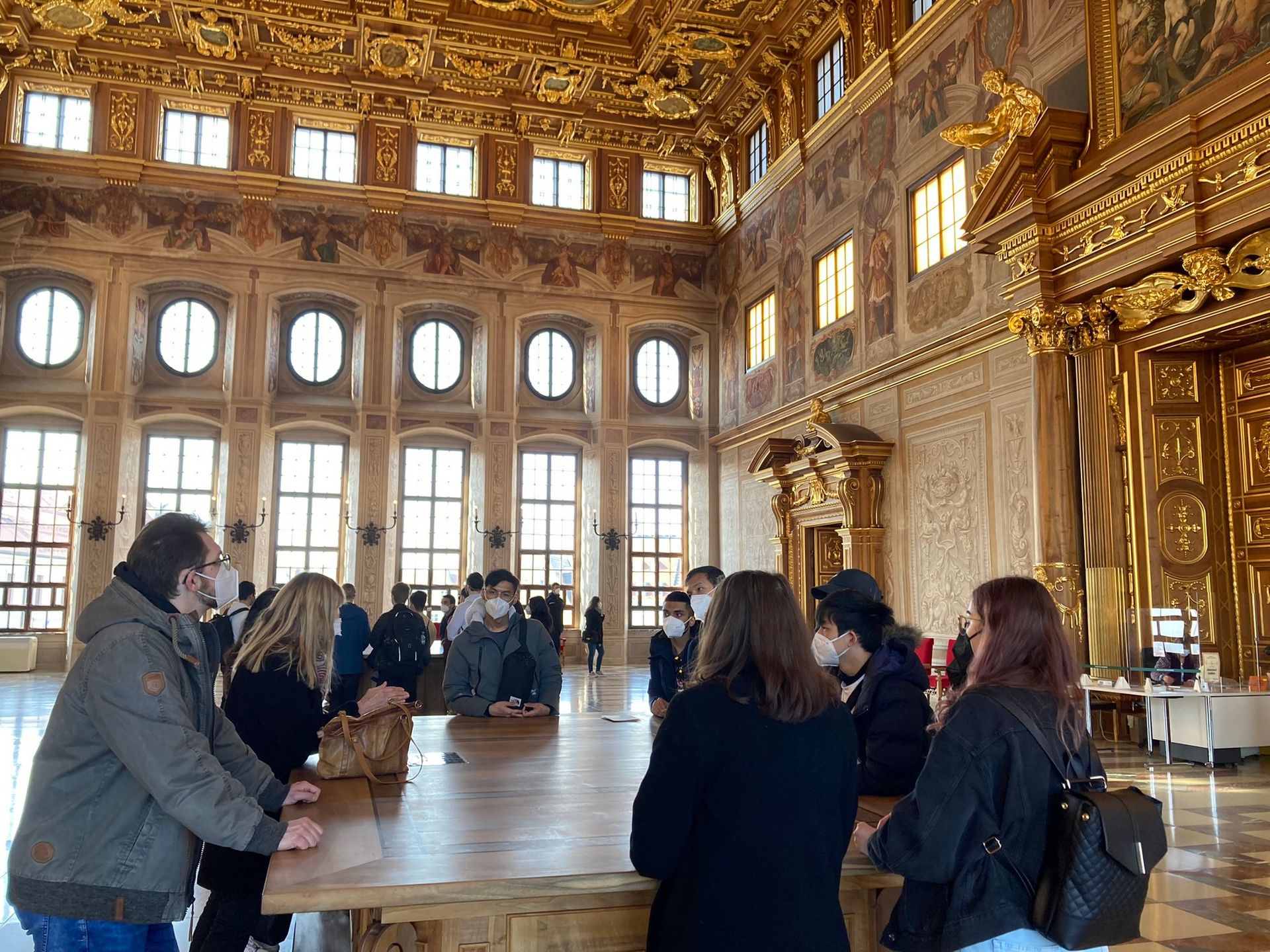 Studierende seteh um einen Tisch herum im goldenen Saal des Augsburger Rathaus