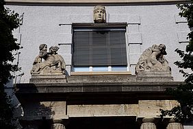 Eine Großansicht eines der historischen Eingänge von Gebäude 1 am Campus Stadtmitte. Es sind die Figuren mit dem Drachen und der Wasserkraft zu sehen.