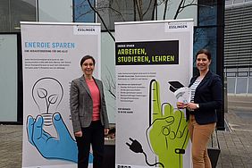Vor zwei Standplakaten zur Energiesparkampagne sind Professor Carla Cimatoribus und Anja Necker zu sehen.