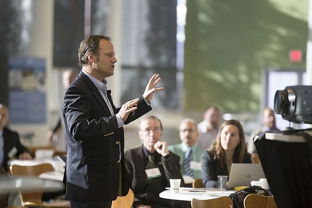 A man gives a lecture with listeners in the background