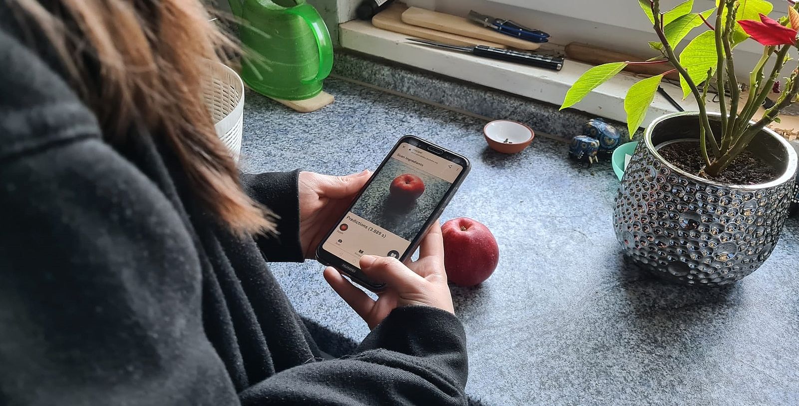 Eine Frau hält ihr Handy über einen Apfel, um mit der Bilderkennung ein Rezept zu finden.