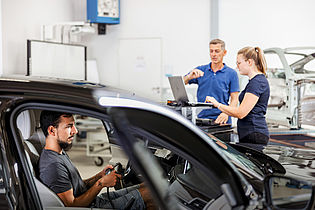 2 persons working with a diagnostic computer one person is sitting in a car