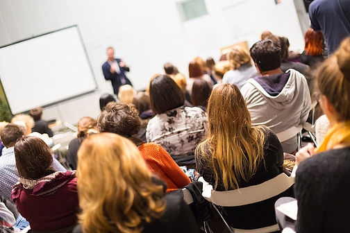 Lecture hall photographed from behind with students and a speaker 