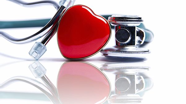 A stethoscope lying on a table with a red plastic heart in the middle 