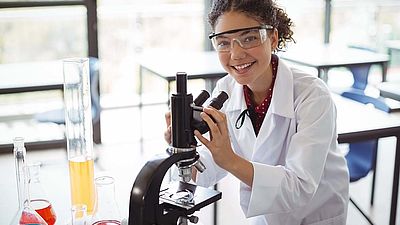Portrait einer Schülerin, die mit einem Mikroskop experimentiert.