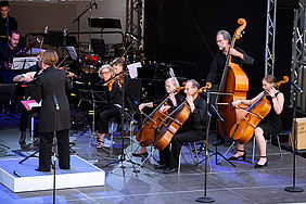 Auf einer Bühne sitzen die Musikerinnen und Musiker des Orchesters und stimmen sich ein.