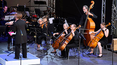 Auf einer Bühne sitzen die Musikerinnen und Musiker des Orchesters und stimmen sich ein.