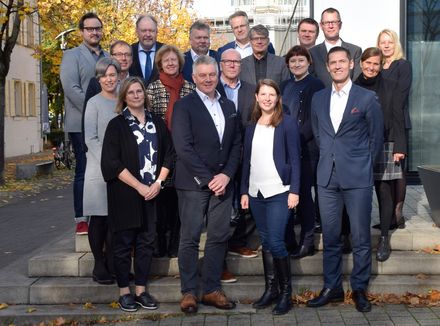 Gruppenfoto von 18 Personen auf einer Treppe vor einem Gebäude.