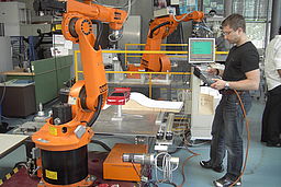 Student vor einem Roboter mit einer Steuerung an der Hand