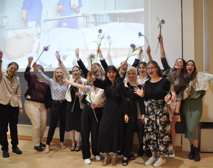 Gruppe von Studierenden hält Blumen in die Höhe und freut sich