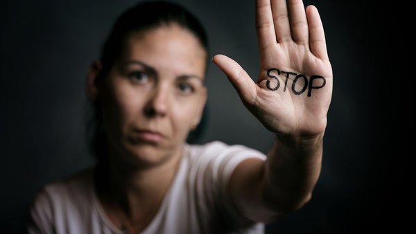 Eine Frau vor schwarzem Hintergrund. Sie h&auml;lt die Hand nach vorne ausgestreckt in der Handfl&auml;che steht STOP geschrieben. Die Handfl&auml;che steht im Fokus.