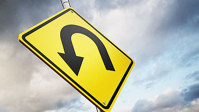 Ein Verkehrsschild welches einen Wenden-Pfeil anzeigt. Der schwarze Pfeil ist auf einem gelben Schild abgebildet. Im Hintergrund ein dunkler Wolkenhimmel.