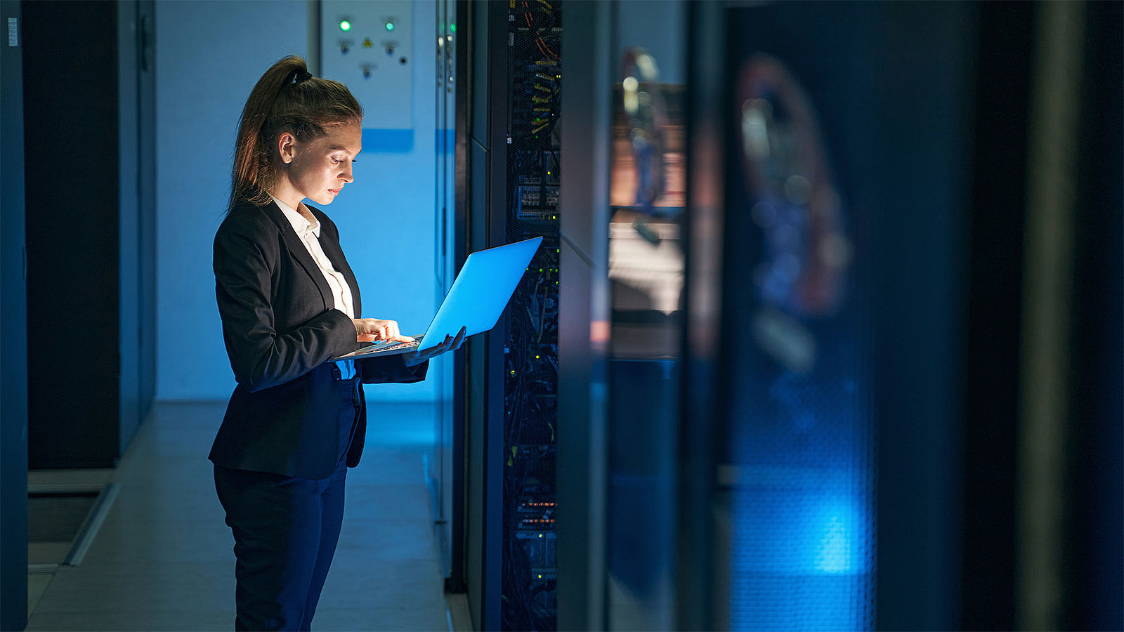 A woman stands in a server room and checks the security of the systems..