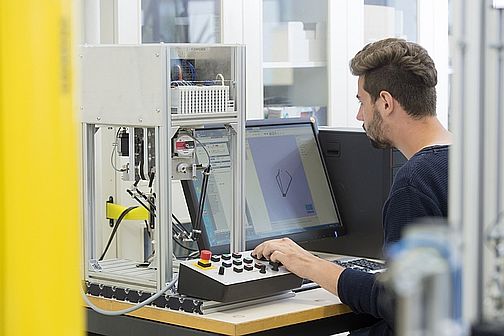 Student im Labor am Computer neben einem Laborgerät