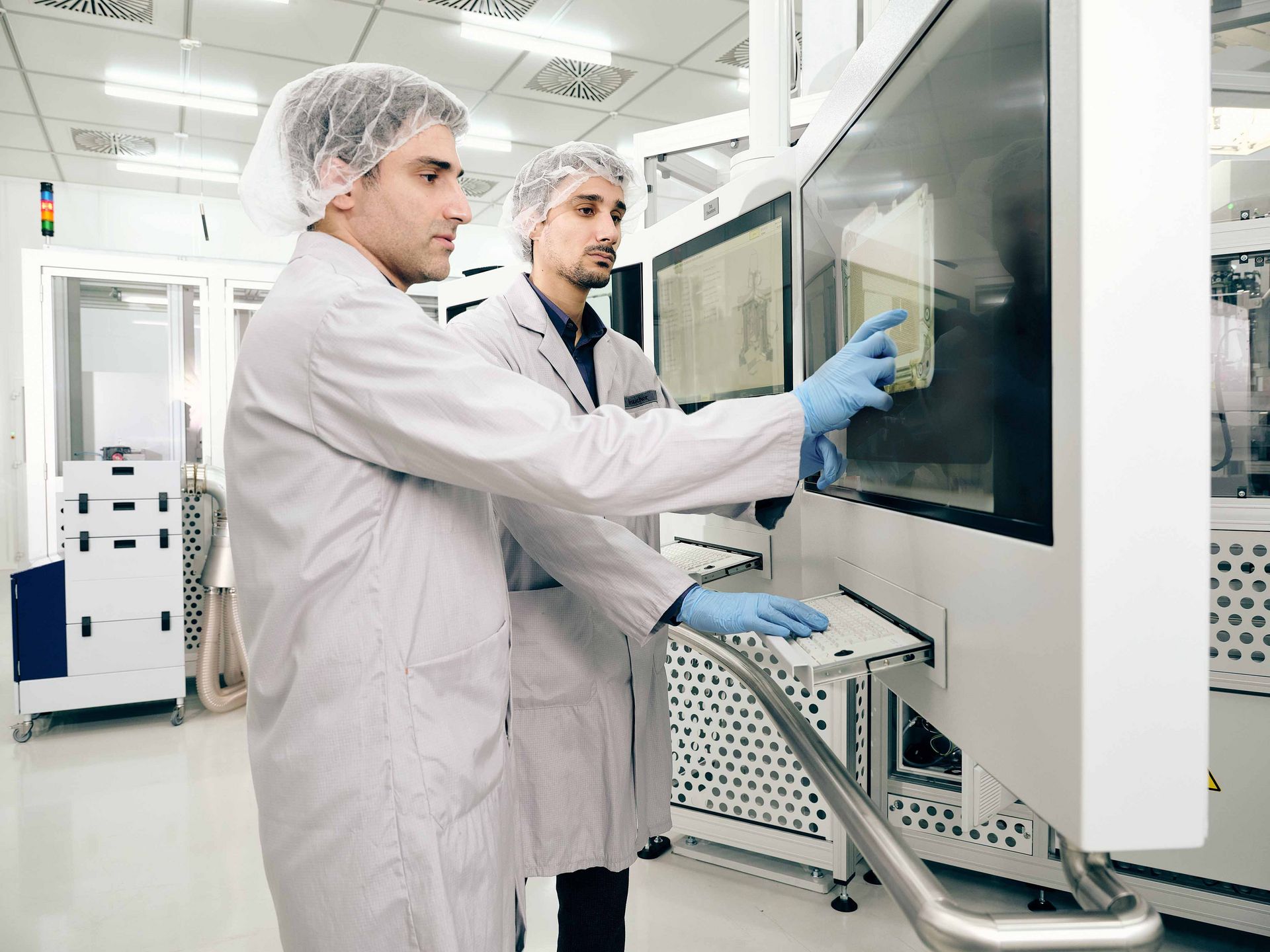 Zwei Männer stehen in weißen Reinraumanzügen in einem Labor und bedienen eine Maschine.
