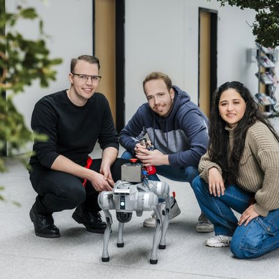 Drei Studierende posieren mit einem Roboterhund.