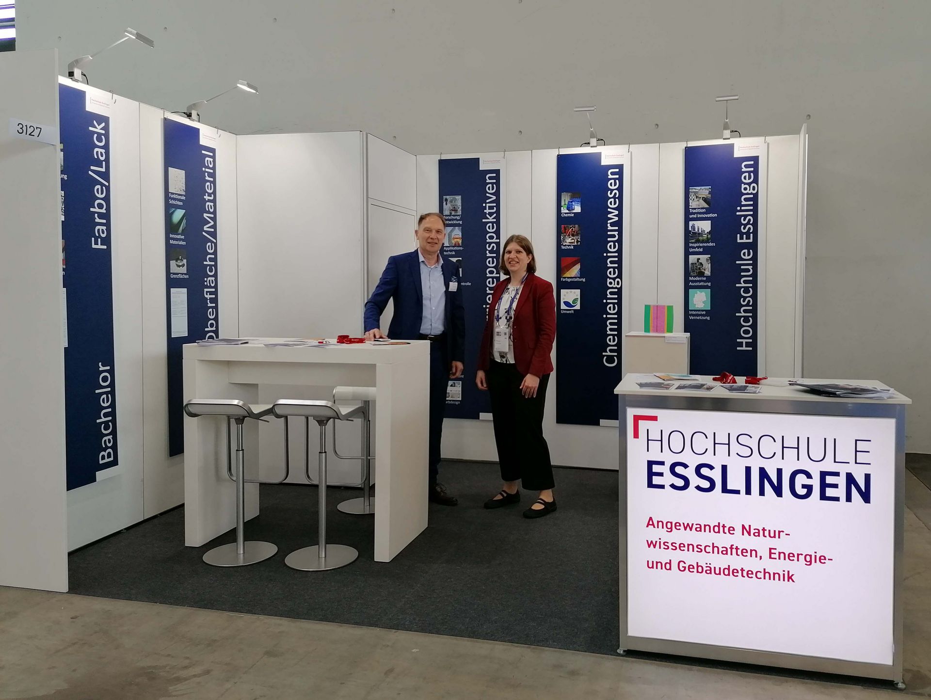 Der Messestand des Studiengangs Chemieingenieurwesen. Zwei Personen stehen hinter einem Tisch mit Flyern, hinter ihnen hängen Plakate.