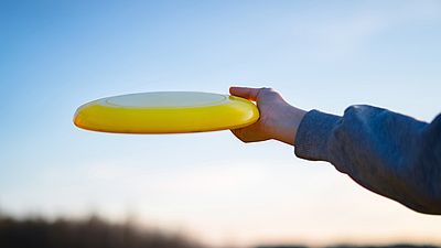 Hand holding yellow frisbee outside. Flaying frisbee outdoors with blue sky in the background