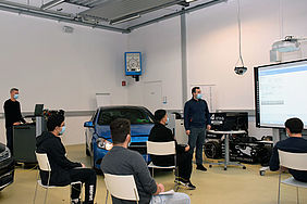 Fünf Studierende und zwei Lehrende in einer Fahrzeughalle.