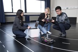 Drei Studierende, die ein selbstgebautes ferngesteuertes Auto bedienen