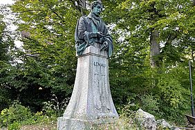 Auf einem Steinsockel in einem Park steht eine Bronzeskulptur von Lenau.