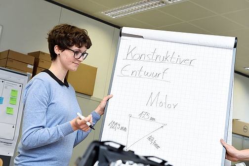 Eine Studentin präsentiert den Entwurf eines Motors vor einer Flipchart.