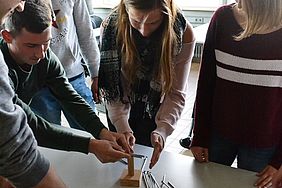Studierende beugen sich über einen Tisch, auf dem Schrauben liegen