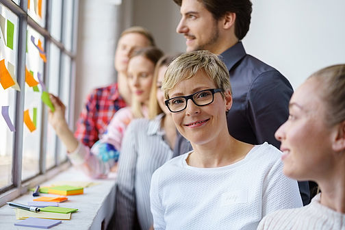 Team von Mitarbeiterinnen und Mitarbeiterinnen - eine Frau schaut in die Kamera