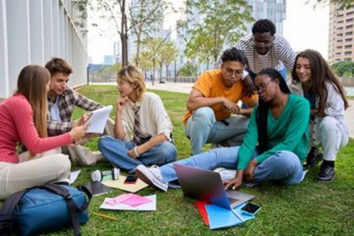 Gruppe internationale Studierende sitzt mit Laptop und Workbook auf der Wiese am Campus