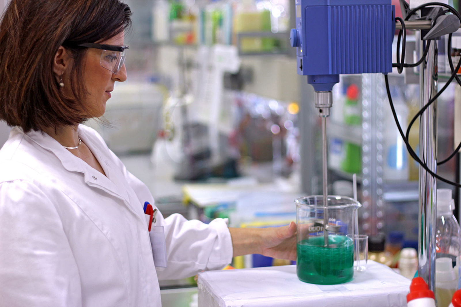 Eine Frau im Labor stellt einen Glasbehälter mit Flüssigkeit auf ein Arbeitsgerät.
