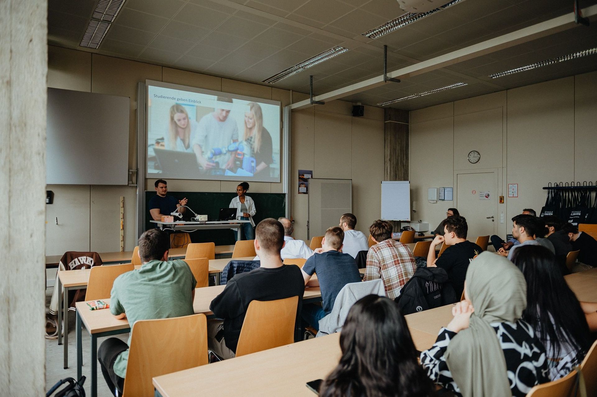Mann und Frau sprechen vor einer Schulklasse
