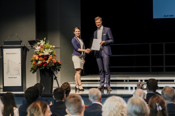 Mann überreicht eine Urkunde an eine Studentin