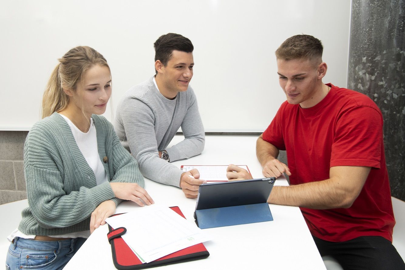 Zwei Männer und eine Frau sitzen an einem Tisch mit Arbeitsmaterial