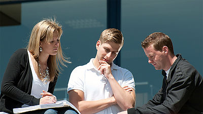 Studenten stehen vor der Hochschule und besprechen Aufgaben. 