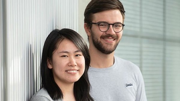 Zwei Studierende an eine Wand gelehnt, lächelnd. 