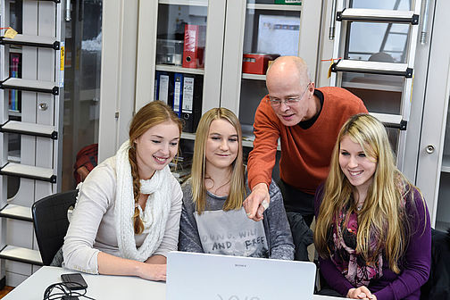 Studierendengruppe arbeitet am Laptop unter Anleitung eines Professors