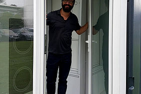 Ein Mann mit Brille öffent die Glastür eines Hauses. 