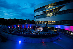 Das Mercedes-Benz-Museum mit der Open-Air Bühne vor einem Abendhimmel.