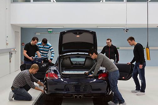 Group of students works on the laboratory vehicle Porsche, hood and doors are open