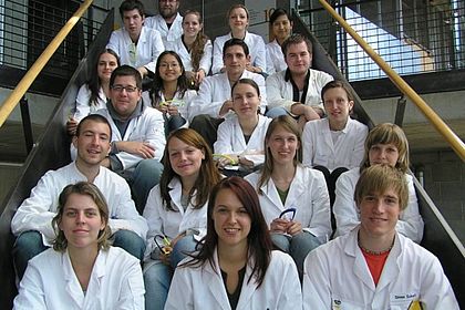 Studenten sitzen in Laborkitteln auf einer Treppe 
