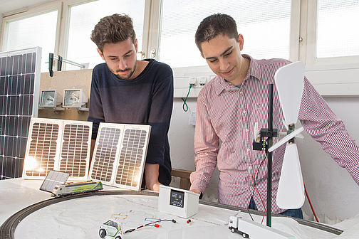 Zwei junge Männer begutachten eine solarbetriebene Modelleisenbahn.