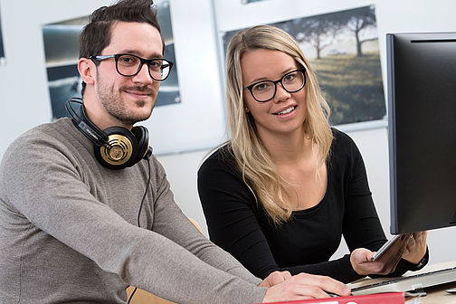 Eine junge Frau und ein junger Mann an einem PC.