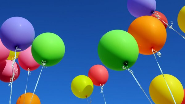 Bunte Luftballons an einer Schnur von unten nach oben in den Himmel fotografiert. Im Hintergrund blauer Himmel zu sehen.