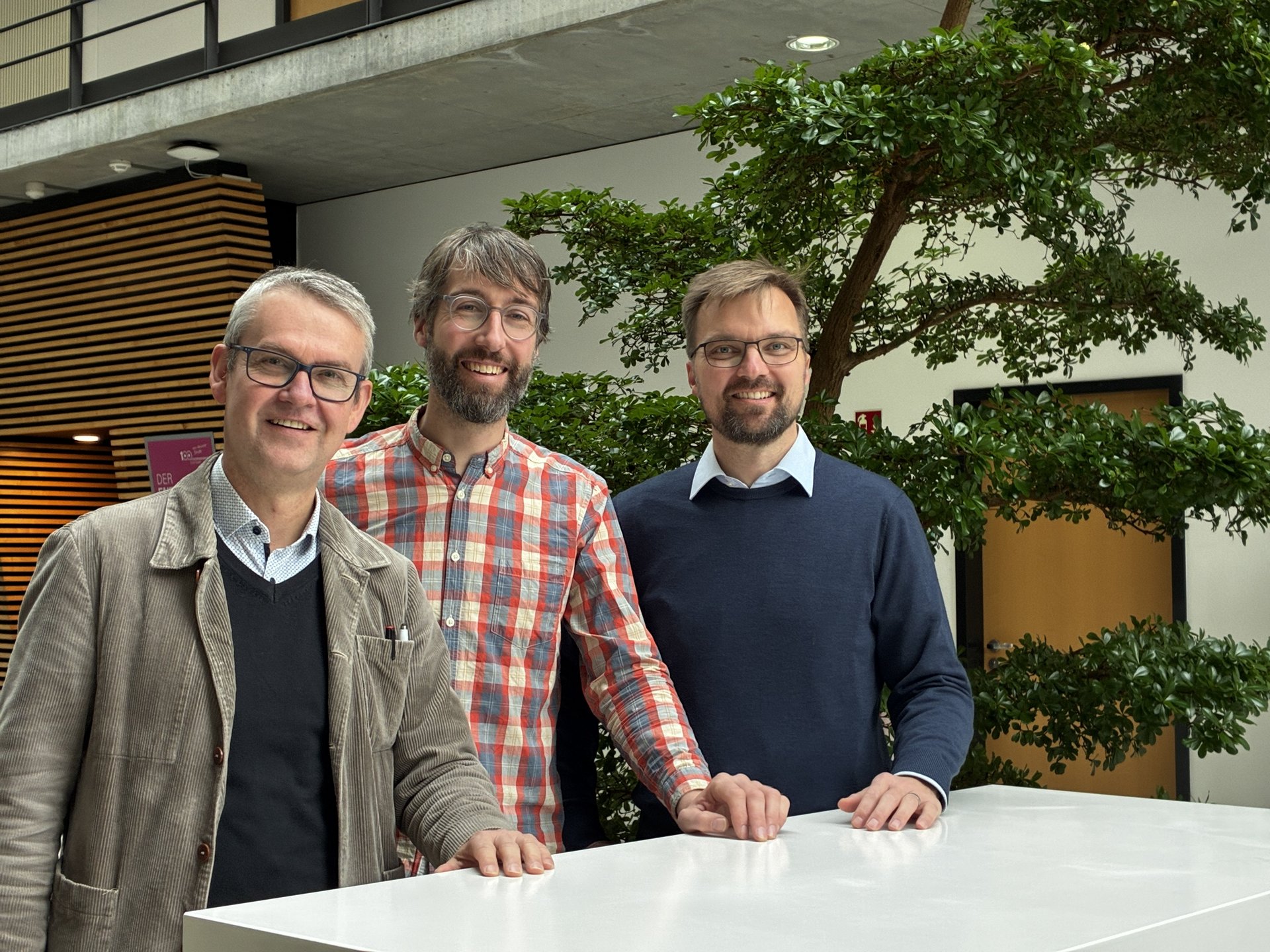 drei M&auml;nner l&auml;cheln in die Kamera