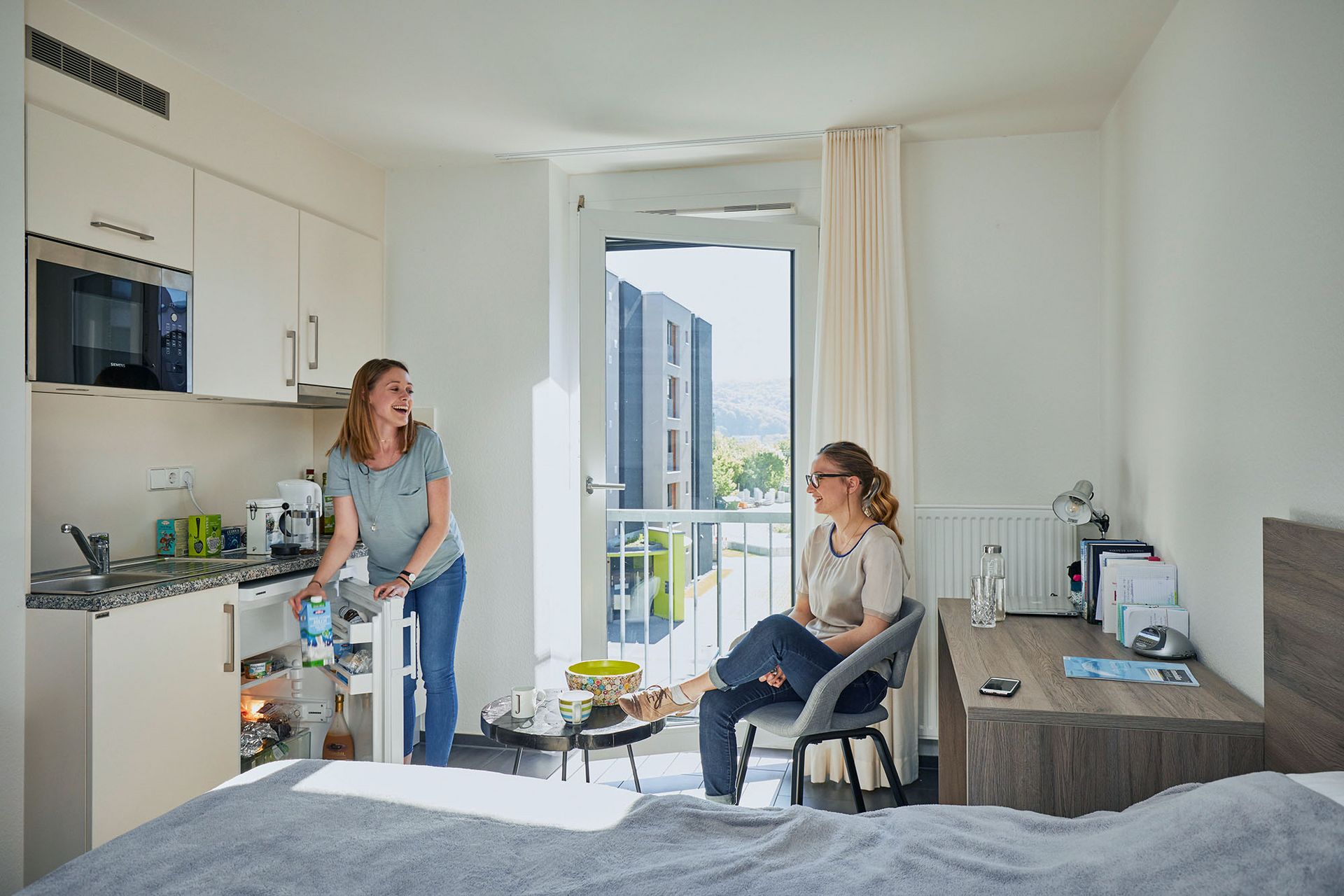 In einem Zimmer einer Wohnanlage des Studierendenwerks Stuttgart sitzen zwei Frauen und unterhalten sich.