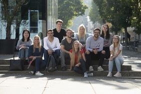 Frauen und Männer sitzen auf einer Treppe auf dem Campus 