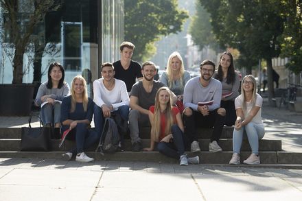 Frauen und Männer sitzen auf einer Treppe auf dem Campus 