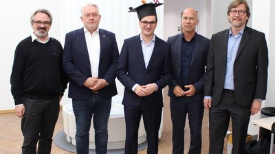 Mann mit Doktorhut steht zusammen mit Professoren