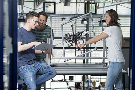 Three students in front of a quadrocopter